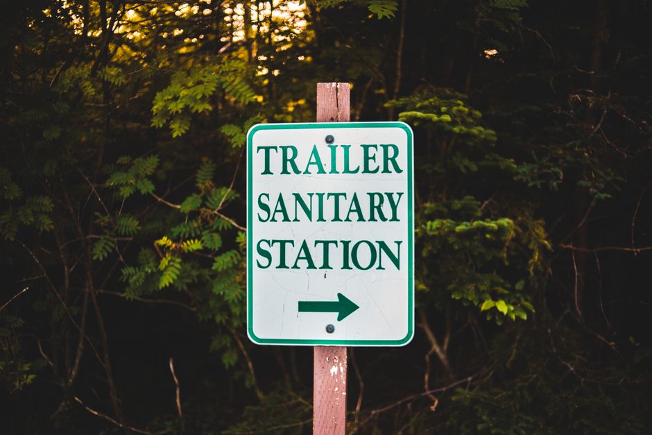 Close-up of a trailer sanitary station sign in a forest, relevant to RV sanitation and toilet odor control.