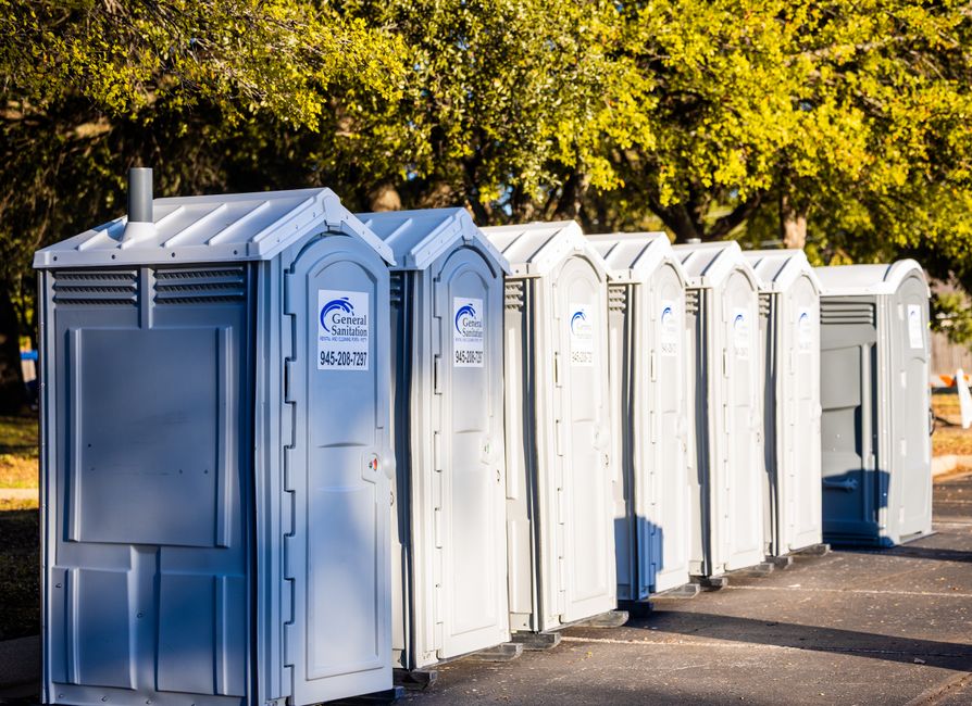 A row of clean portable toilets lined up outdoors under trees, ready for a multi-day event rental in Eastern Idaho.